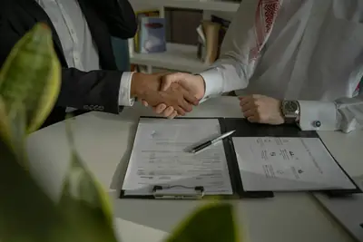 Two people shaking hands over a printed job offer and contract on a desk