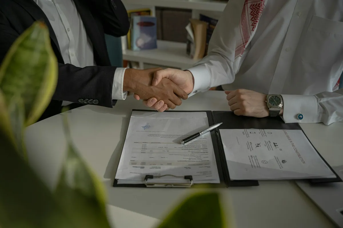 Two people shaking hands over a printed job offer and contract on a desk