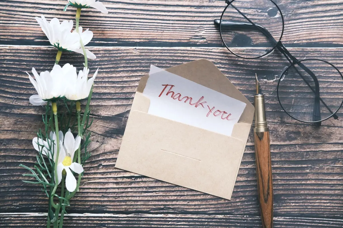 Handwritten thank-you note in a kraft envelope next to a pen and glasses