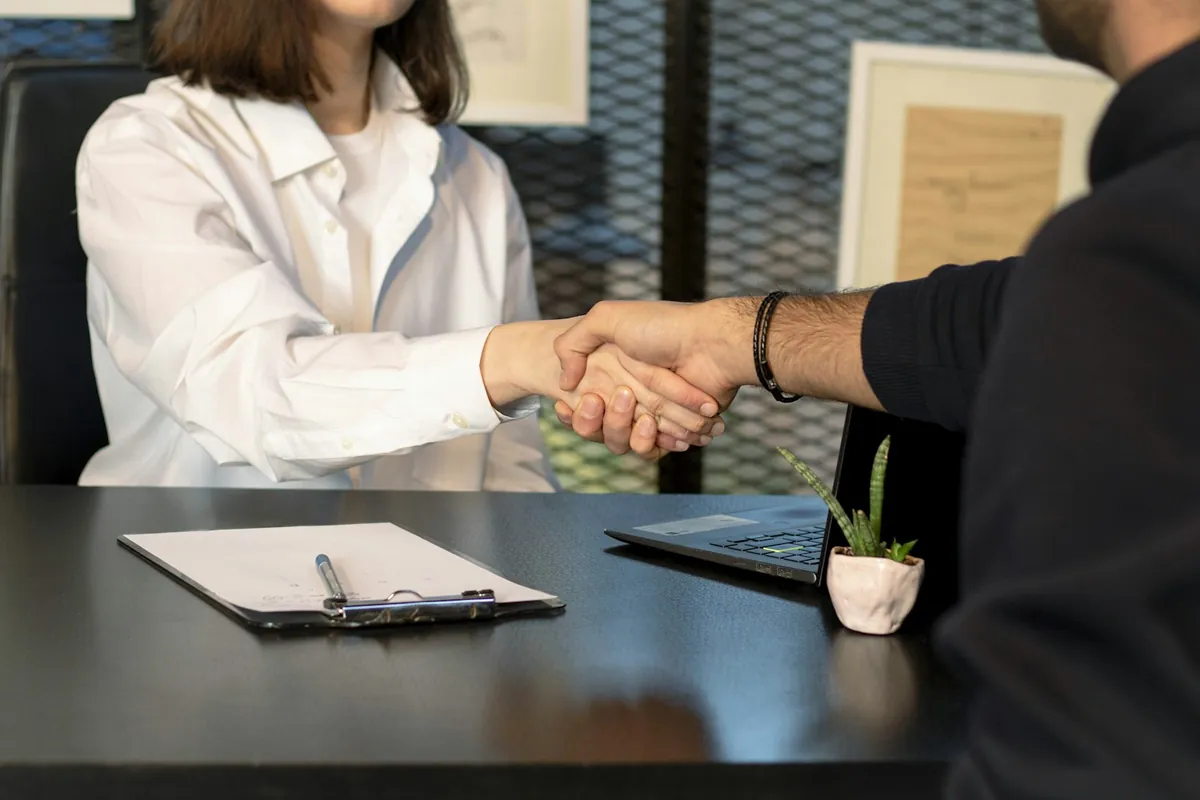 Interviewer and candidate shaking hands across a desk after a behavioral interview